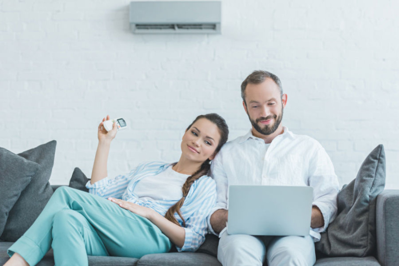 couple sitting on a couch, using their remote to adjust their ductless ac unit.