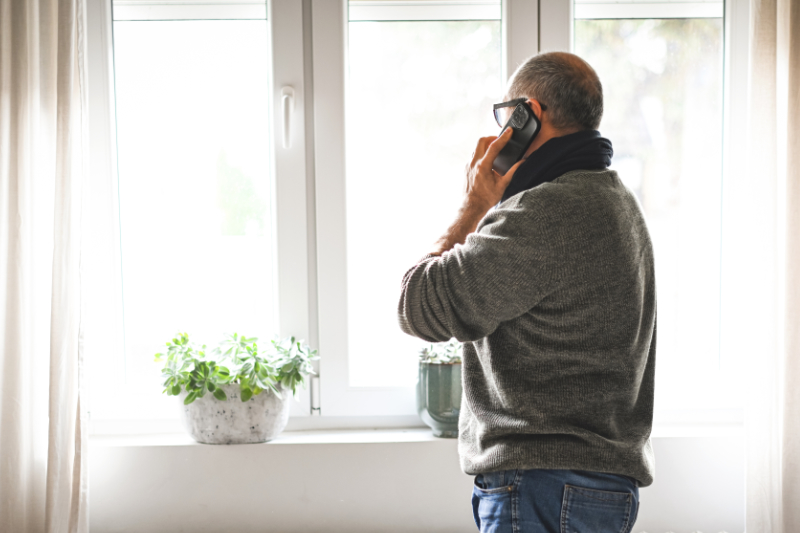 Why Won’t My Furnace Stop Running? Photo of a man looking out of a window while on his phone.