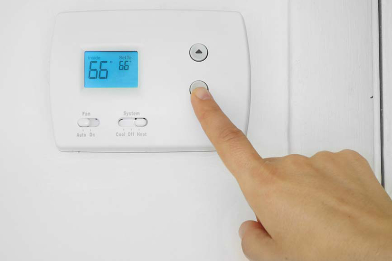 5 Reasons Why Regular HVAC Maintenance is Essential for Berrien County Homeowners. Image is a photograph of a person's hand adjusting a wall mounted thermostat temperature.